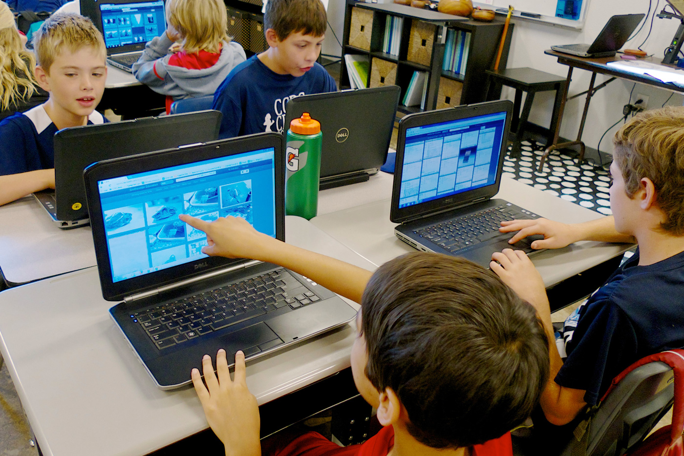 Four students sit at a desk with laptops interacting with the prototype for the Learning Lab. One student in the foreground points at his screen.