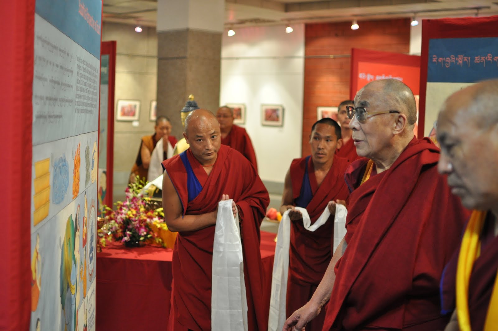 His Holiness the 14th Dalai Lama of Tibet and other monks, dressed in red, view one of the panels of the World of Your Senses exhibition