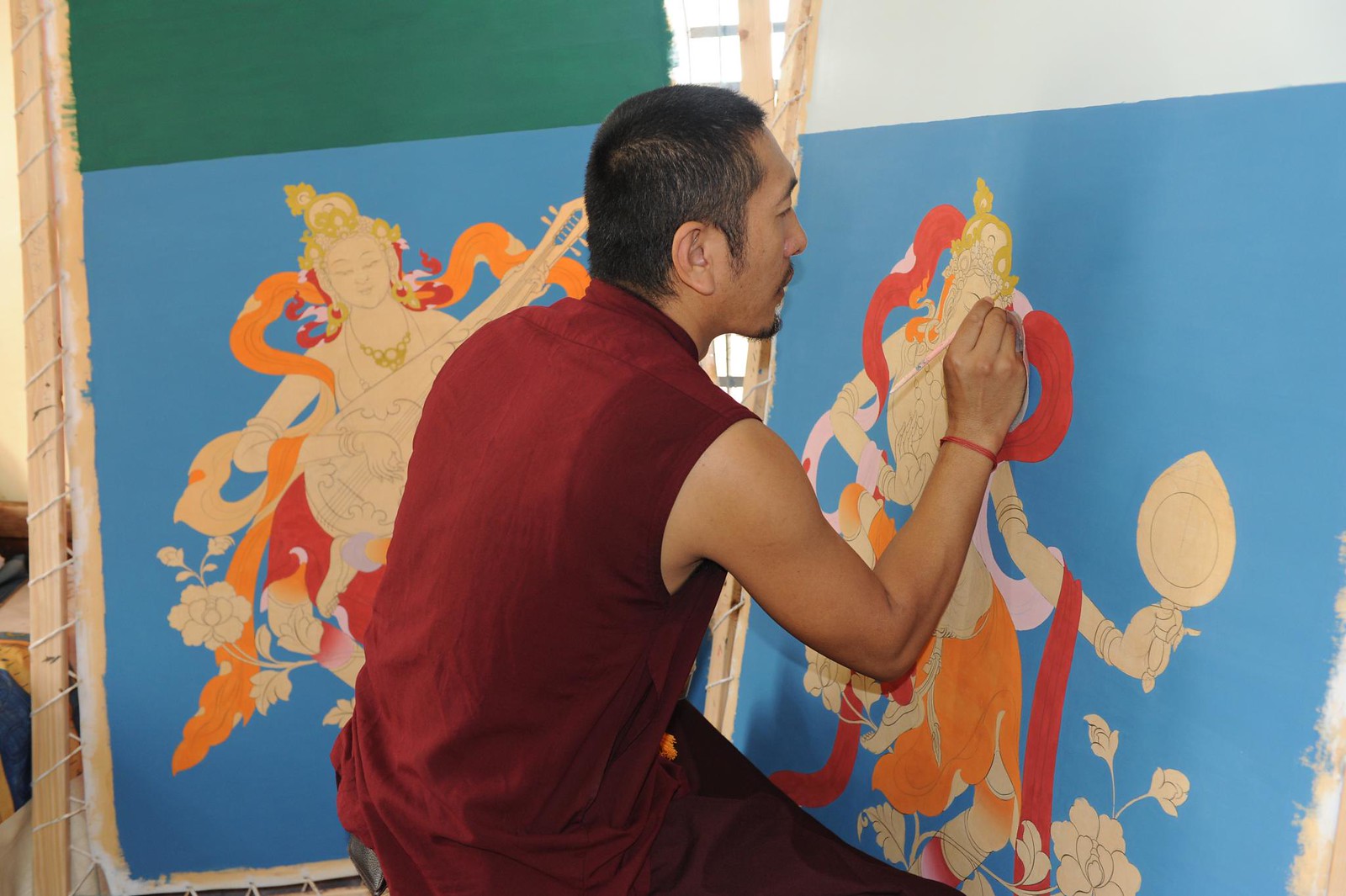 A thangka artist sits in front of a large canvas with a large sections of blue color.
